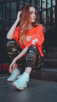 Fashion model wearing red hoodie with the inscription los angeles posing in the city at parking. Fashion urban outfit. Casual everyday clothing style