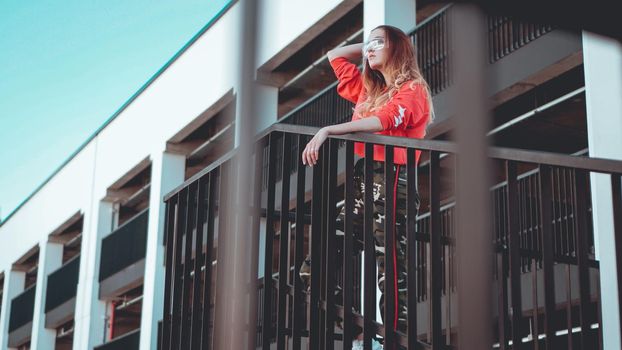 Fashion model wearing red hoodie with the inscription los angeles posing in the city at parking. Fashion urban outfit. Casual everyday clothing style