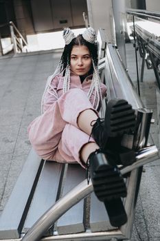 Young woman with futuristic looks. Girl with black and white dreadlocks or pigtails. Against the background of a futuristic building
