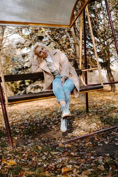 Portrait of smilling middle aged woman sitting and swinging on swing in autumn park