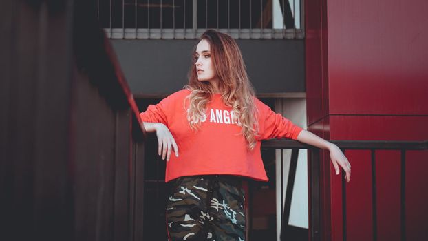 Fashion model wearing red hoodie with the inscription los angeles posing in the city at parking. Fashion urban outfit. Casual everyday clothing style