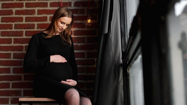 Young pretty pregnant woman in black dress in studio - loft interior