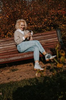 Beautiful middle aged woman using smart phone outdoors - autumn park