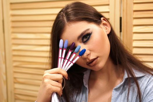 Beautiful girl with blue makeup covers her face with a palette with nails for manicure