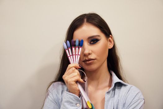 Beautiful girl with blue makeup covers her face with a palette with nails for manicure