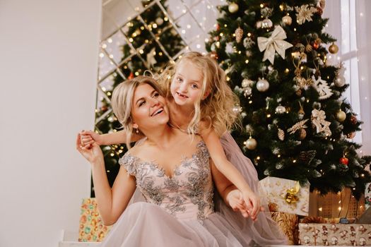 Smiling daughter hugging her mother while sitting at christmas tree with gift boxes