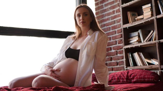 Beautiful young stylish pregnant woman in black lingerie and white shirt, in the interior of a loft