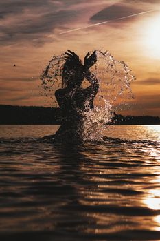 Young model swimming in the sea - sunset time. Feminine, attractive silhouette with spray