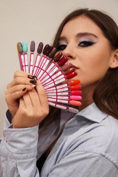 Beautiful girl with blue makeup covers her face with a palette with nails for manicure