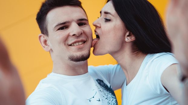 Handsome man with beautiful sexy woman licking man cheek on yellow background