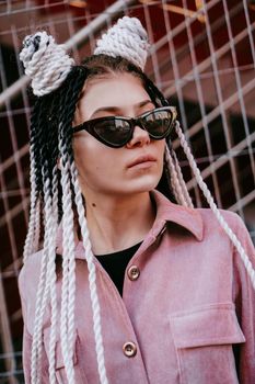 Portrait of beautiful cool girl over urban wall. Sunny day. Girl in sunglasses and pink jumpsuit