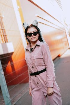 Portrait of beautiful cool girl over urban wall. Sunny day. Girl in sunglasses and pink jumpsuit