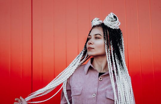 Portrait of beautiful cool girl with Senegalese pigtails and dreadlocks over red wall