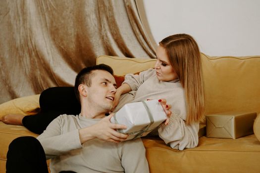 Beautiful young couple holding a gift box while sitting on couch at home - soft preset