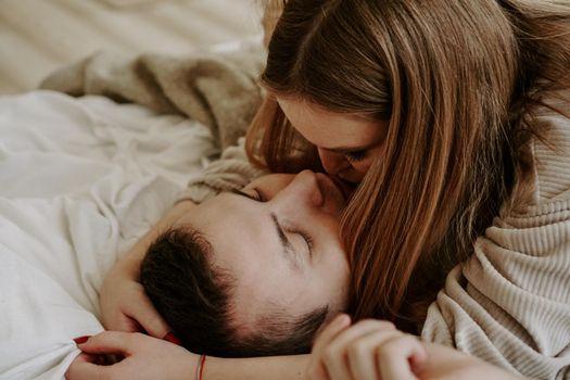 Close-up portrait of a beautiful young kissing couple in bed at home. Soft colors