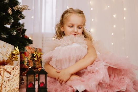 Girl in a pink dress near the Christmas tree and boxes with gifts