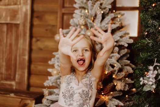Happy Little girl in a pink dress grimaces on the background of the Christmas tree