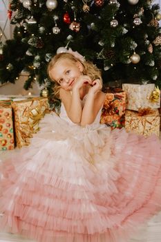 Girl in a pink dress near the Christmas tree and boxes with gifts