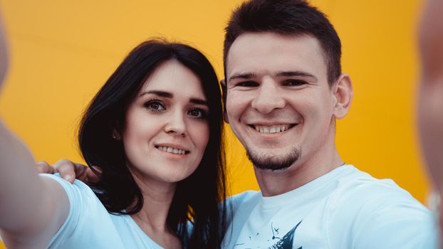 Young lovely couple posing together while making selfie over yellow background