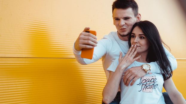 Young lovely couple posing together while making selfie on smartphone over yellow background