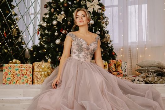 Christmas, winter holidays concept. Beautiful woman in evening long dress posing in luxurious apartments decorated for Christmas. Beauty, fashion.