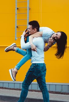 Happy man carrying his girlfriend on yellow background - couple in love
