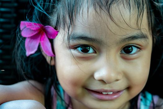 Little girl with large pink flower behind ear. Pretty asian child portrait with flower behind ear smiling