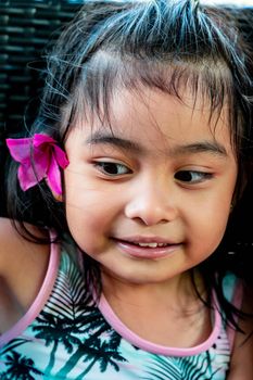 Little girl with large pink flower behind ear. Pretty asian child portrait with flower behind ear smiling