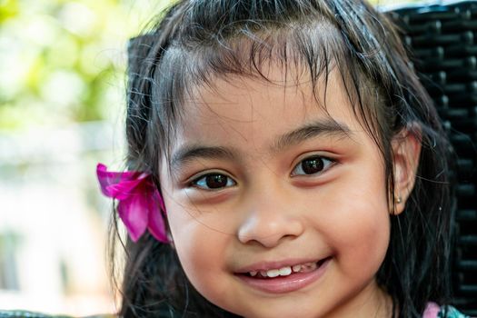 Little girl with large pink flower behind ear. Pretty asian child portrait with flower behind ear smiling
