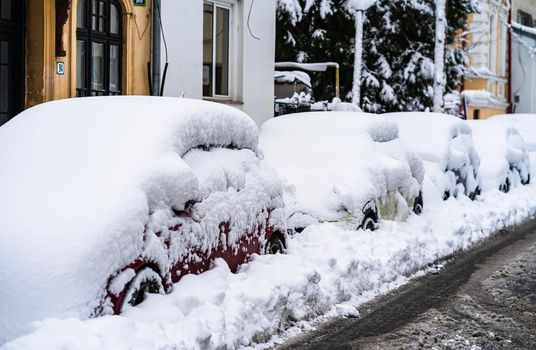 Cars covered with snow from the first snow fall of the year. Winter concept, snowy cars parked on the street, deep layer of snow