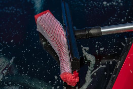 Washing and cleaning the front window of a car with mop in self service car wash station, close up isolated.