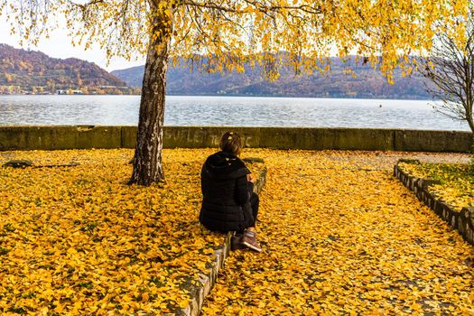 Autumn leaves fallen on standing alone woman on the autumn alley. Autumn landscape, orange foliage in a park in Orsova, Romania, 2020