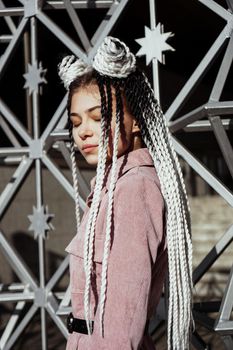 Young woman with futuristic looks. Girl with black and white dreadlocks or pigtails. Against the background of a futuristic building