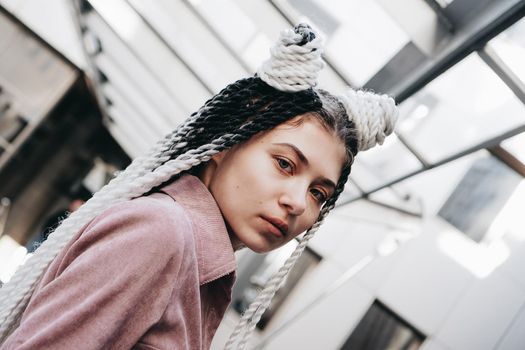 Young woman with futuristic looks. Girl with black and white dreadlocks or pigtails. Against the background of a futuristic building