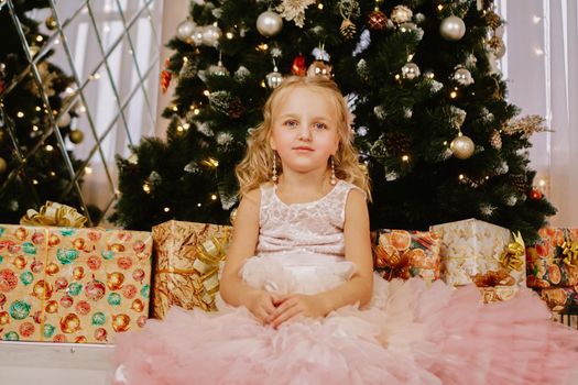 Girl in a pink dress near the Christmas tree and boxes with gifts