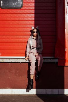 Beautiful girl over urban wall. Sunny day. Girl in sunglasses and pink jumpsuit