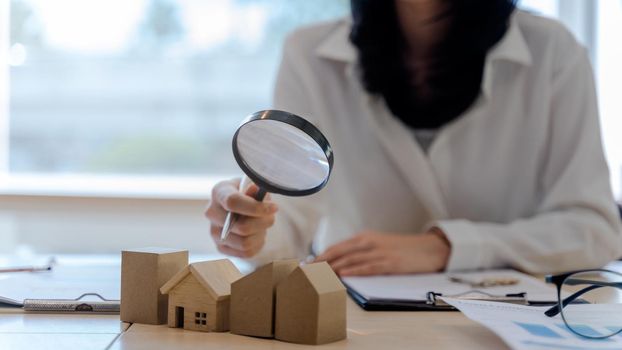 Assessor woman or realtor agents use a magnifying glass to checking house model. Concept of real estate and house appraisal.