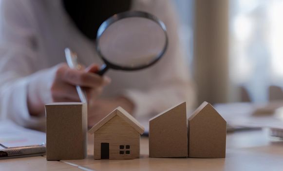 Woman bank officer or appraiser using magnifying glass to check miniatures house model. The concept of searching for living and checking quality inspection of housing or assets.