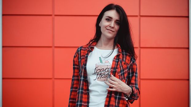 Portrait of beautiful young woman in red plaid shirt and white tshirt with a print without logos. Background of a red wall