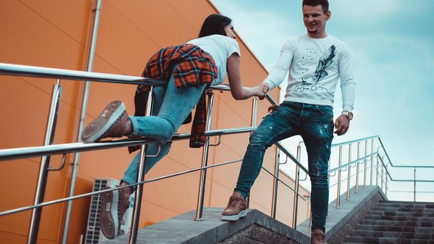 Young smiling couple in love man holding attractive woman hand, spending time together, enjoying - orange background - girl rolls on the railing