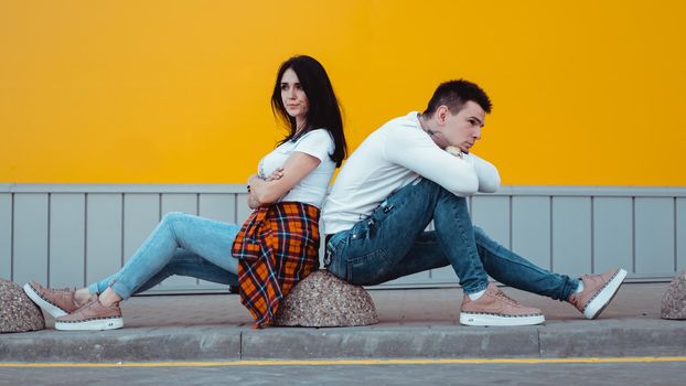 Confused young couple standing with one anothers back with crossed arms over yellow background