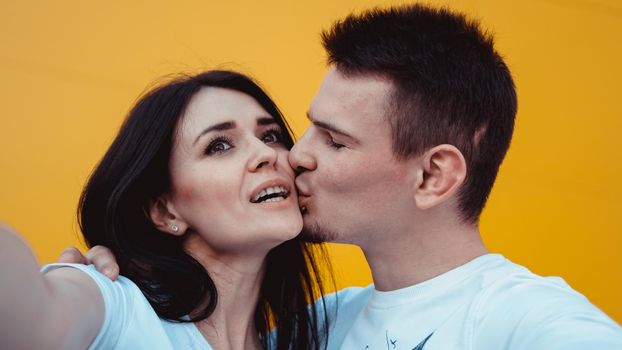 Young lovely couple posing together while making selfie on smartphone over yellow background