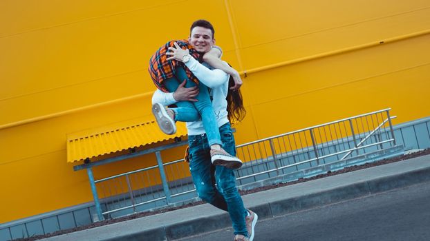 Happy man carrying his girlfriend on yellow background - couple in love