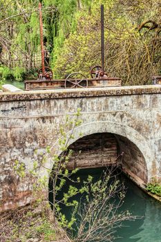 The Jucar River and old stone bridge surrounded by vegetation in Alcala del Jucar village