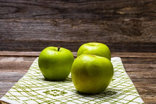 Ripe green apples on a rustic napkin on wooden table.