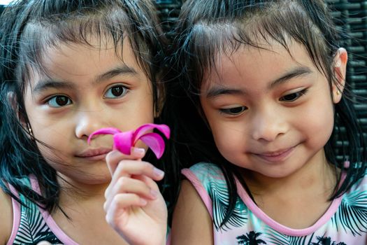 Pretty child twins holding a pink flower. Pretty asian twins portrait with flower and smiling