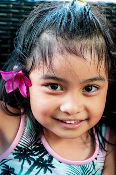 Little girl with large pink flower behind ear. Pretty asian child portrait with flower behind ear smiling