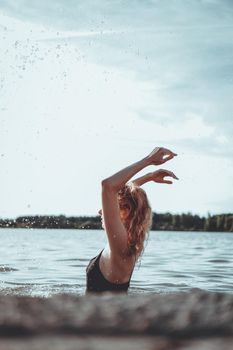 Young beautiful woman standing in the water. Black swimsuit. Vintage style. vertical photo