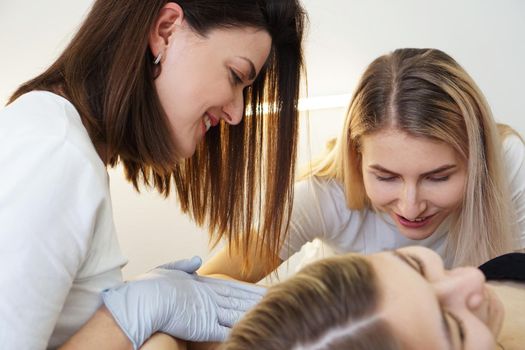 Two cheerful confident cosmetologists doing hair removal. Two happy women do the armpit depilation procedure. The concept of teaching depilation