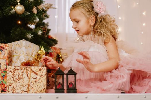 Girl in a pink dress near the Christmas tree and boxes with gifts